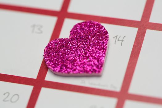 Close up of pink glittery heart marking valentines day on white and pink calendar
