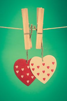 Two heart ornaments hanging from pegs on a line on green background