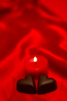 Chocolate hearts and lit candle on red silk