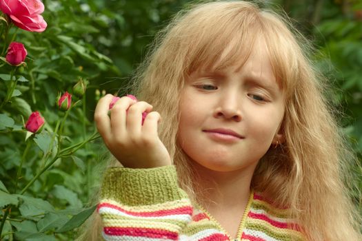Beautiful small Caucasian girl in park near the flowering rose bush