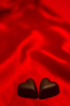 Two chocolate hearts on red silk background
