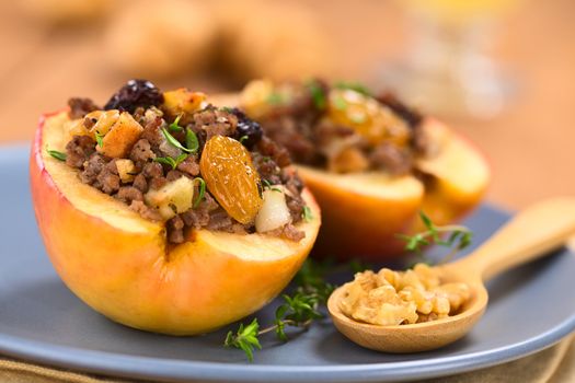 Savory baked apple filled with mincemeat, raisins, sultanas, onion and walnut, sprinkled with fresh thyme leaves on top served on blue plate with walnuts on wooden spoon  (Selective Focus, Focus on the sultana in the front)   