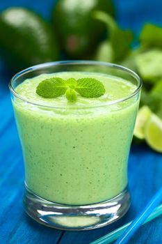 Healthy refreshing green smoothie made of fresh avocado, spinach, lime and yoghurt garnished with mint and served in a glass on blue wood (Selective Focus, Focus on the big mint leaves on the drink)