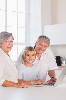 Grandparents and child looking at camera with a laptop in kitchen