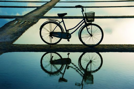 Bicycle put on surface water, water surface like mirror that reflect it's shadow. The sky very nice appeared on watel, lines in horizontal create abstraction