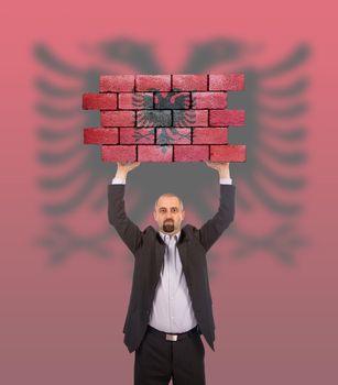Businessman holding a large piece of a brick wall, flag of Albania, isolated on national flag
