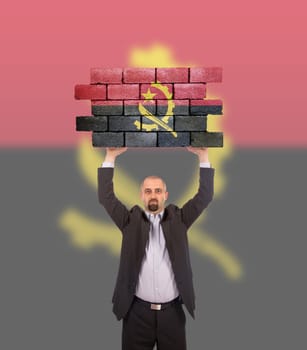Businessman holding a large piece of a brick wall, flag of Angola, isolated on national flag