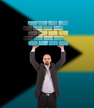 Businessman holding a large piece of a brick wall, flag of the Bahamas, isolated on national flag