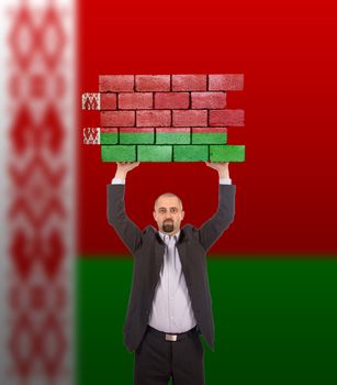 Businessman holding a large piece of a brick wall, flag of Belarus, isolated on national flag