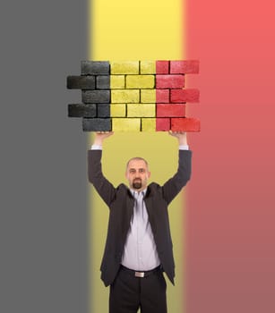 Businessman holding a large piece of a brick wall, flag of Belgium, isolated on national flag
