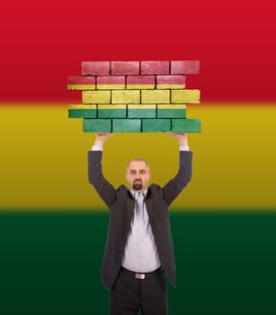Businessman holding a large piece of a brick wall, flag of Bolivia, isolated on national flag