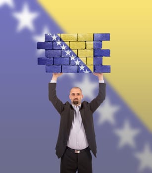 Businessman holding a large piece of a brick wall, flag of Bosnia and Herzegovina, isolated on national flag