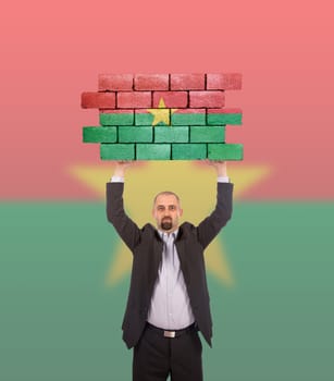 Businessman holding a large piece of a brick wall, flag of Burkina Faso, isolated on national flag