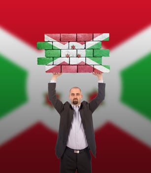 Businessman holding a large piece of a brick wall, flag of Burundi, isolated on national flag
