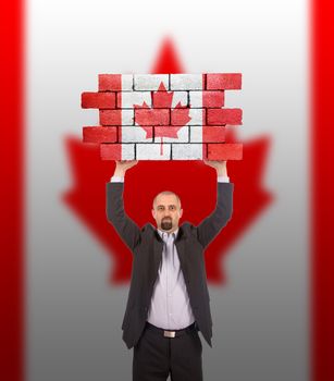 Businessman holding a large piece of a brick wall, flag of Canada, isolated on national flag