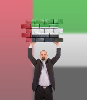 Businessman holding a large piece of a brick wall, flag of the United Arab Emirates, isolated on national flag