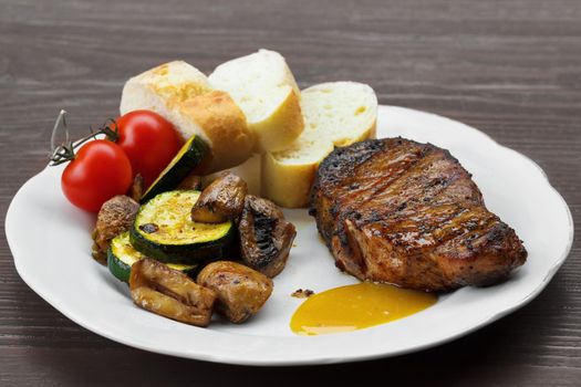 pork steak with sauce, mustard and grilled vegetables on the plate