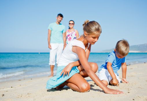 Family of four having fun on tropical beach - two cute kids playing with sand