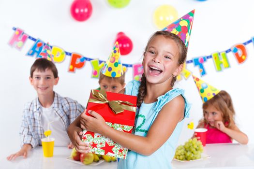 Beautiful girl with giftbox looking at camera having fun at birthday party with his friends on background