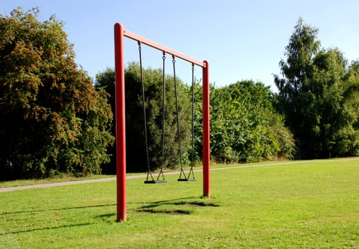 Two swings on a red frame at a park on a sunny day