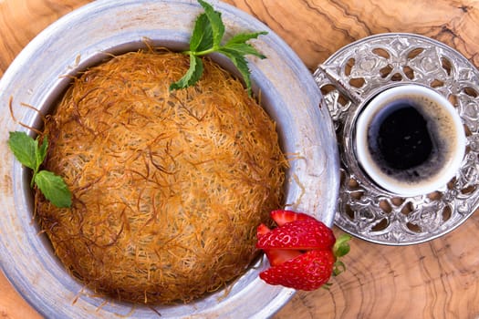 Turkish dessert kunefe isolated on a olive tree table with mints and sliced strawberry along with Turkish coffee