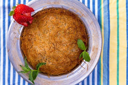 Turkish dessert kunefe isolated on a picnic cloth with mints and sliced strawberry