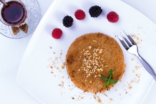 Turkish dessert kunefe  served on a white plate with mint leaves and sliced strawberry along red and black berries