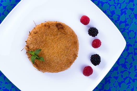 Turkish dessert kunefe on a blue table cloth with mint leaves and berries