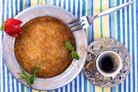 Turkish dessert kunefe isolated on a picnic cloth with mints and sliced strawberry along with Turkish coffee