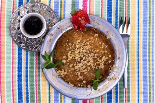 Turkish dessert kunefe on a picnic cloth with mint leaves and sliced strawberry along with Turkish coffee and fork