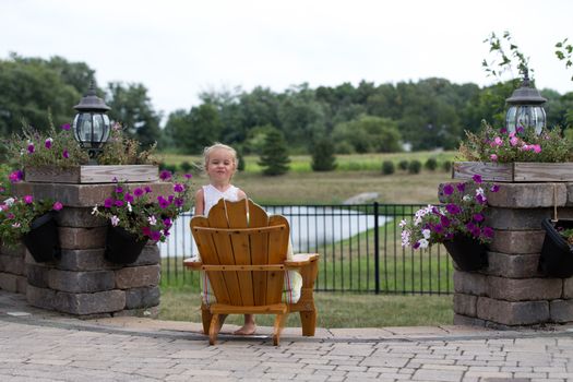 Little blonde smiling from a garden chair  back to the camera overlooking open countryside and a small lake on a brick patio