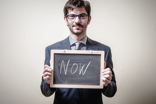 businessman holding blackboard written now on gray background
