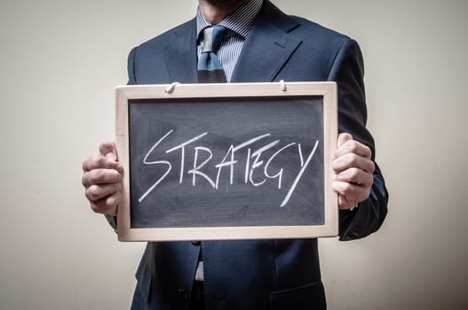 businessman holding blackboard written strategy on gray background