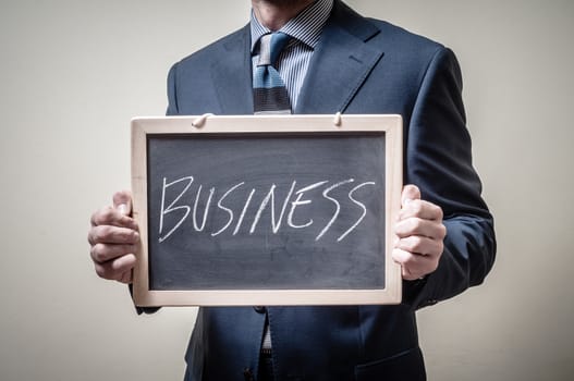 businessman holding blackboard written business on gray background
