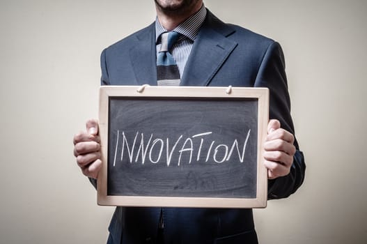 businessman holding blackboard written innovation on gray background