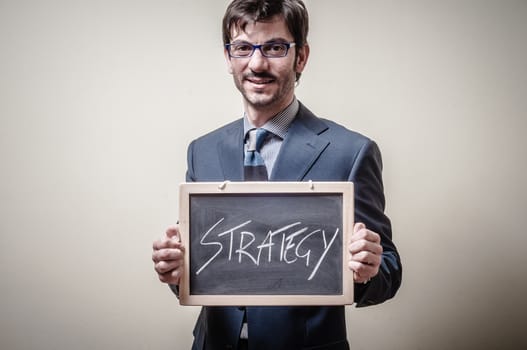 businessman holding blackboard written strategy on gray background