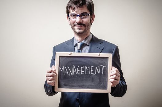businessman holding blackboard written management on gray background