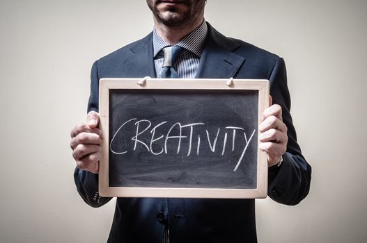 businessman holding blackboard written creativity on gray background