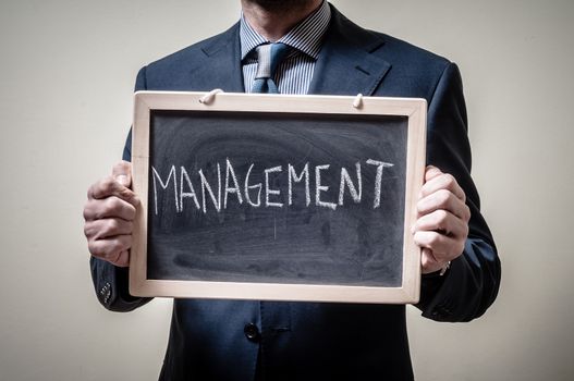 businessman holding blackboard written management on gray background