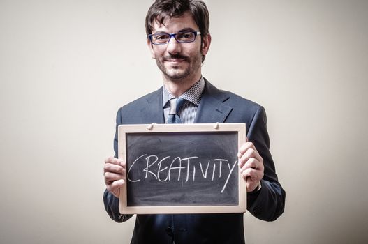 businessman holding blackboard written creativity on gray background