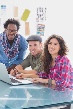 Creative team working together on laptop and smiling at camera at desk in the office