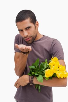 Handsome man blowing a kiss and holding yellow roses on white background