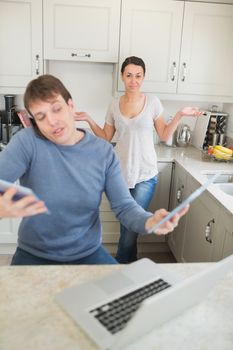 Man busy with technology while his wife wondering why in kitchen