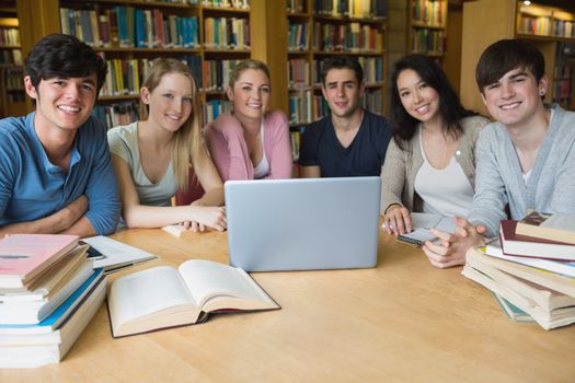 Group of students sitting at a table in a library while using the laptop and learning