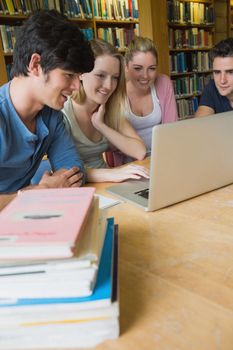 Four students sitting at a desk in a library, while learning and using a laptop