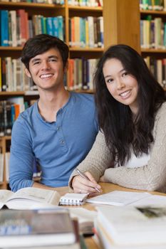 Two people sitting in a library at a desk and learning while smiling