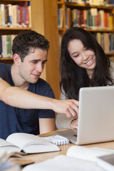 Two students sitting at a desk in a library while having fun and using the laptop