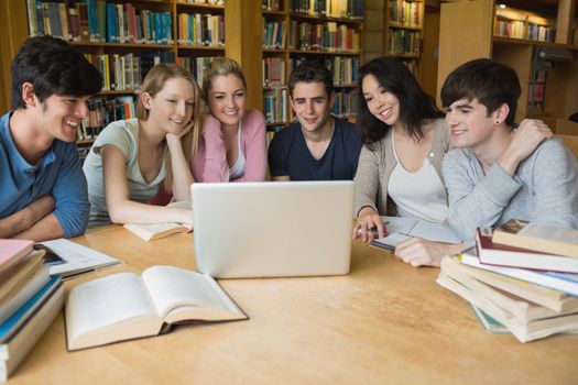 Group of students sitting at a table in a library while learning and using the laptop