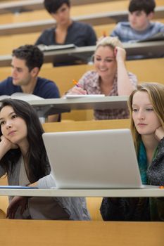 Listening students sitting in a lecture hall while taking notes and working with the laptop