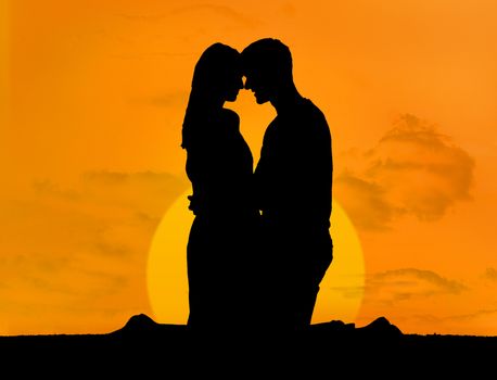 Silhouette of couple embracing under a sunset kneeling face to face